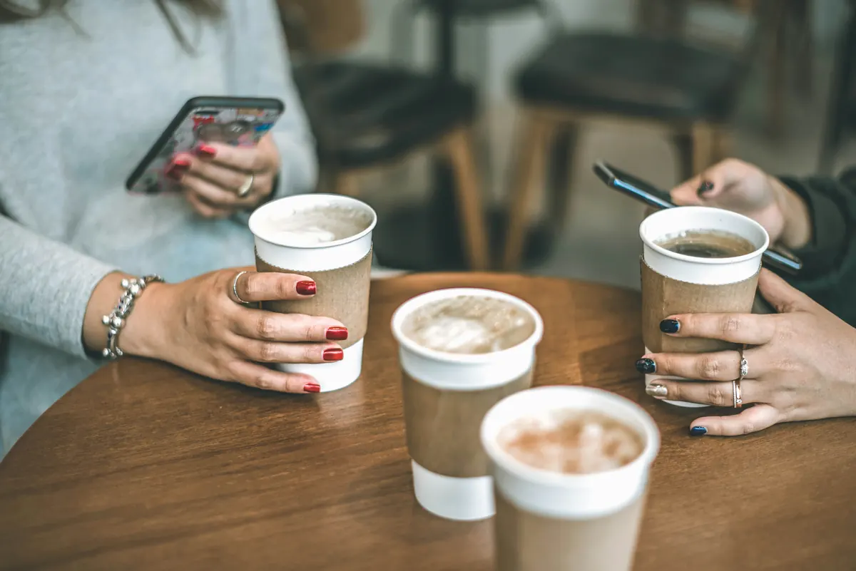 Hands around coffee cups on a café table, two of them holding phones.