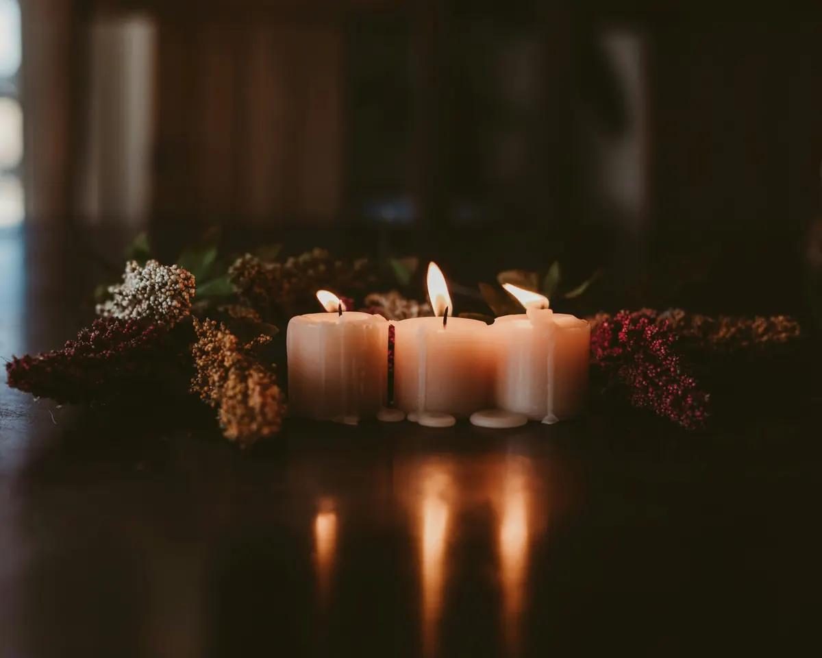 Three lit candles among dried flowers on a dark polished table.