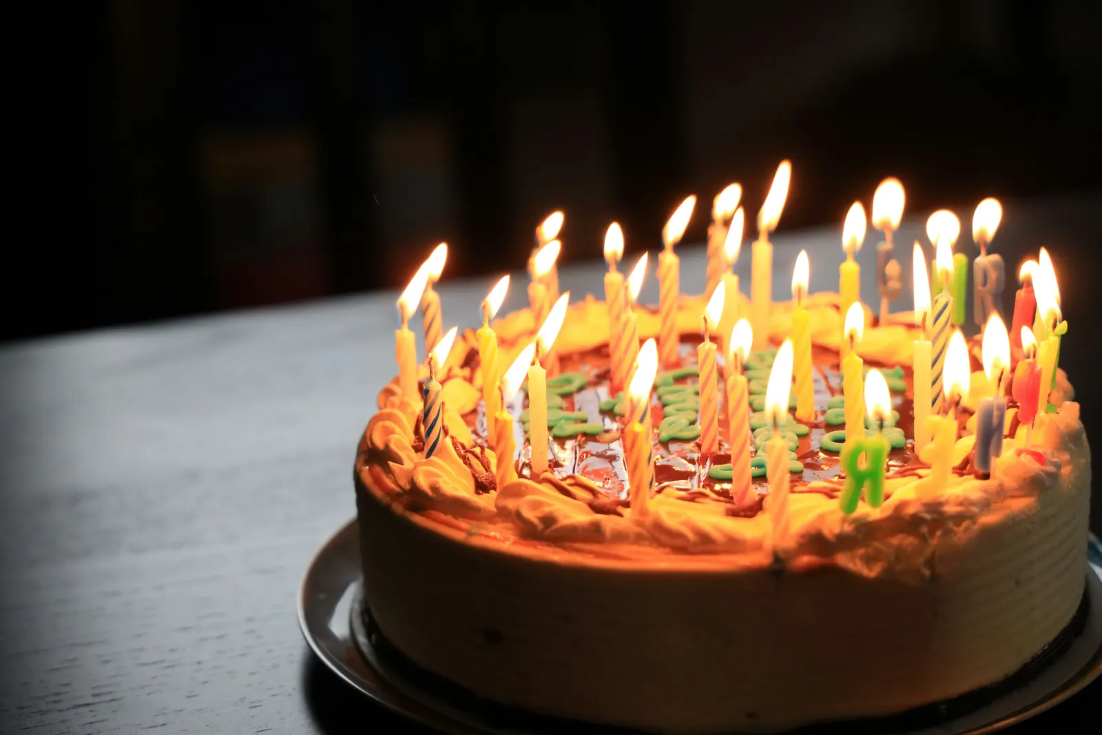 A birthday cake covered in lit candles, glowing in a dark room.
