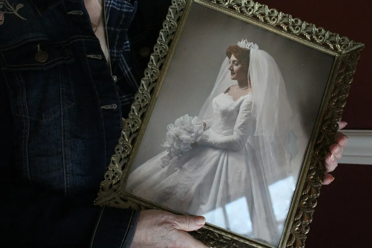 Hands holding an old framed wedding portrait of a bride in her veil.