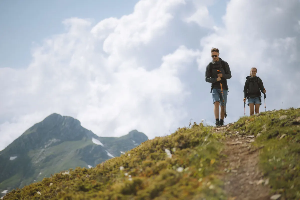 Two hikers walking up a grassy ridge with mountains behind