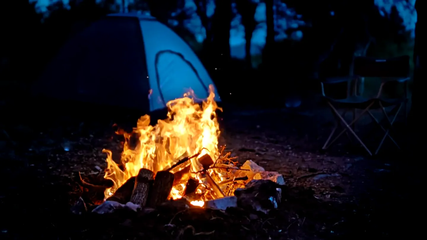 A frame from a finished film: a video clip of a campfire burning beside a tent at night.